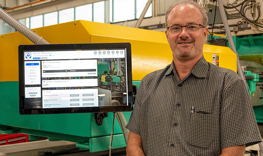 A person standing beside a MOLI touchscreen kiosk mounted on an injection molding press
