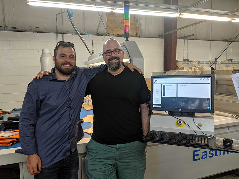 Jake and Steve standing at cutting machine with MOLI screen in foreground and Andon stack light in background