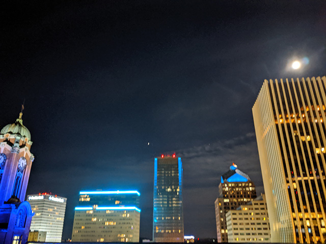 The NextCorps rooftop deck at night with downtown Rochester lit in blue